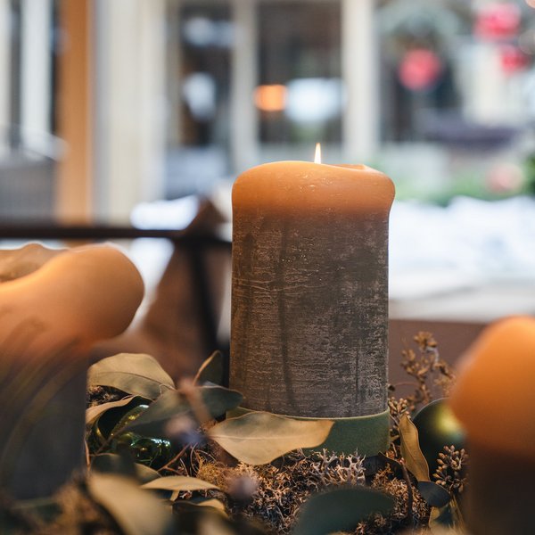 Sensoria Dolomites: il vostro hotel sull’Alpe di Siusi Tre candele accese su decorazioni natalizie con corona verde e piuma di pavone