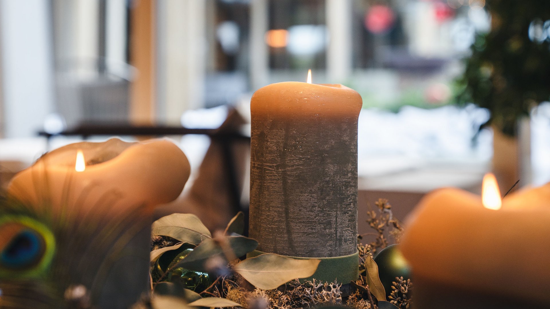 Größte Hochalm Europas – ein Kraftplatz mit Seele Drei brennende Kerzen auf weihnachtlichem Dekor mit grünem Kranz und Pfauenfeder