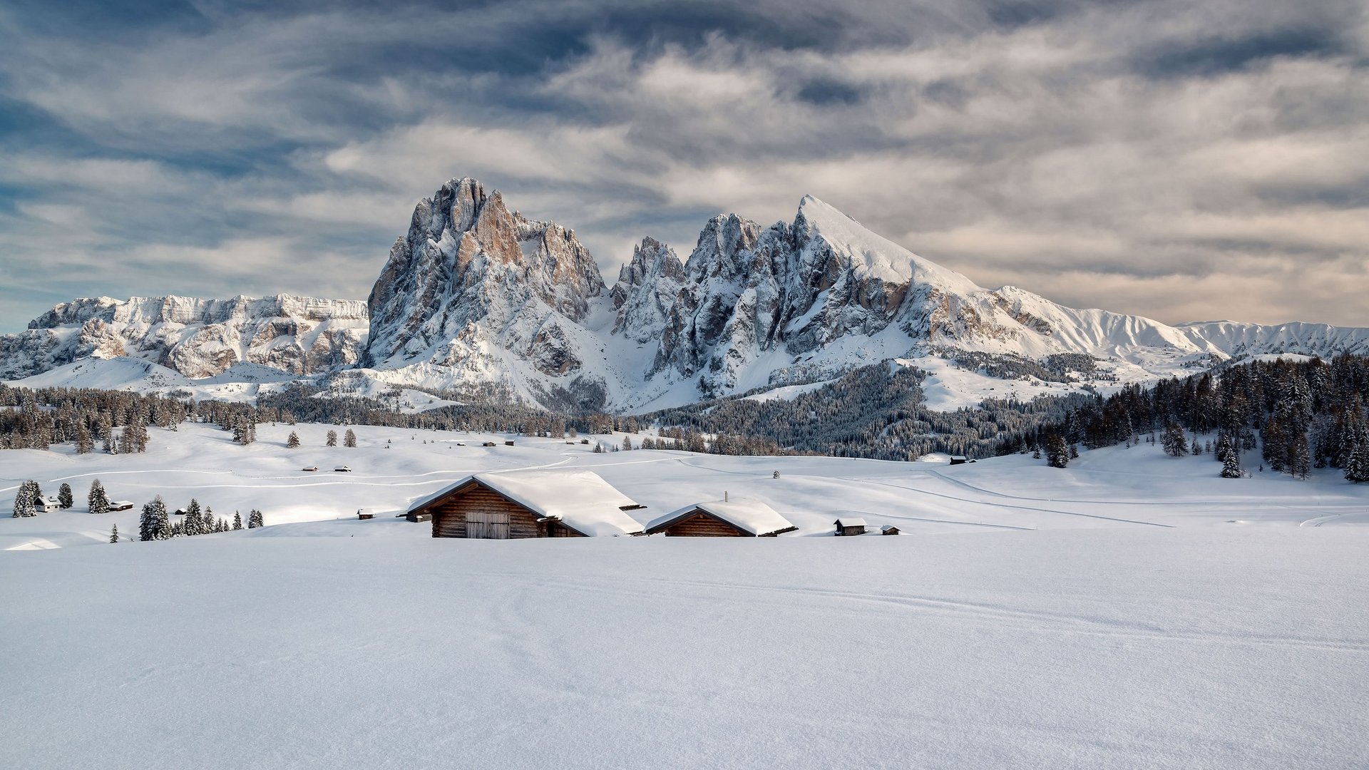 Baite innevate davanti a montagne frastagliate sotto un cielo nuvoloso