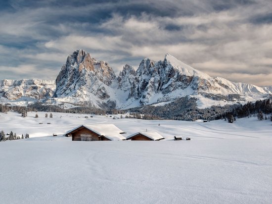 Hotel in Seis am Schlern gesucht? Sensoria Dolomites gefunden! Verschneite Hütten vor schroffen Bergen unter bewölktem Himmel