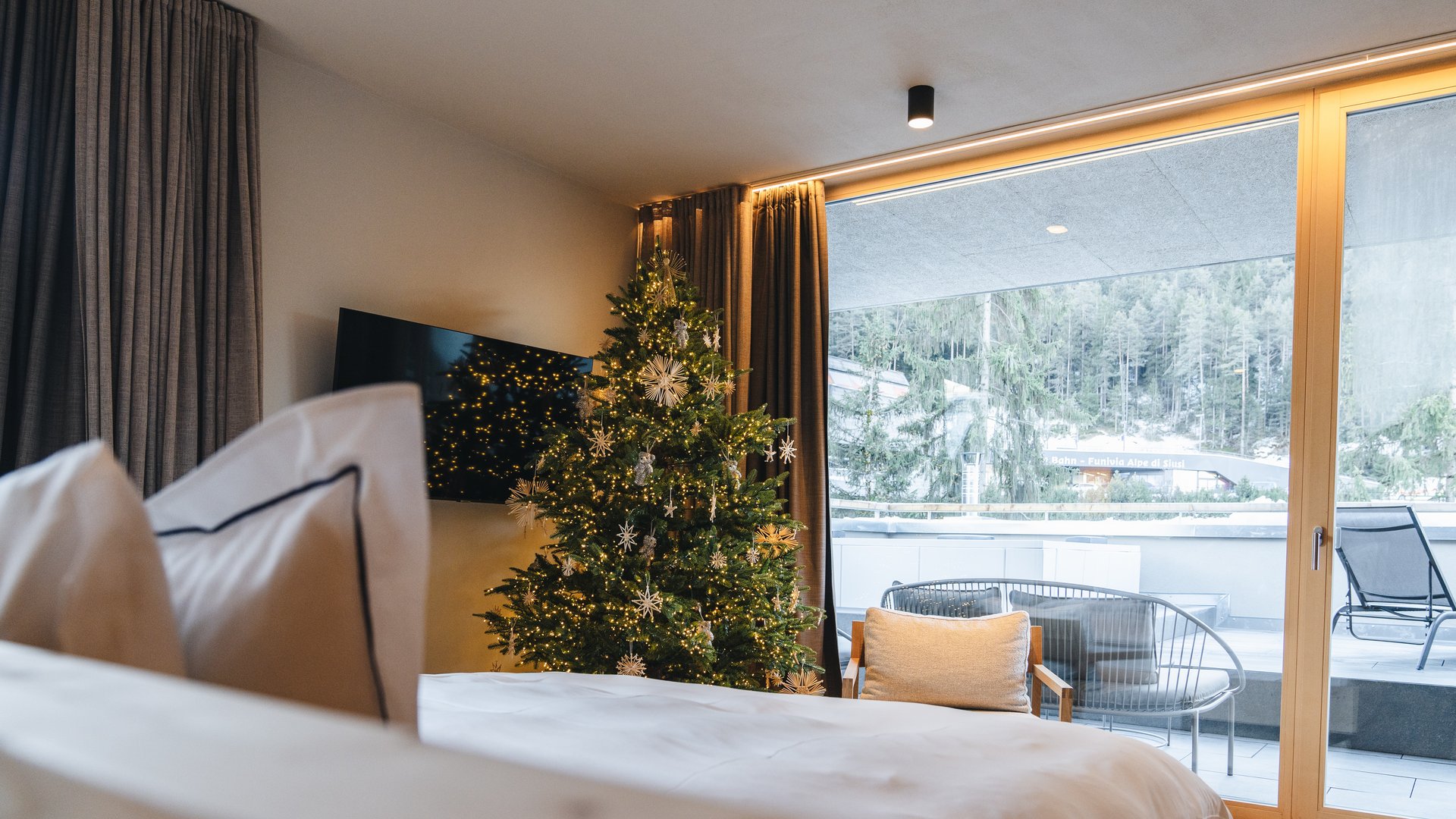 Sensoria Dolomites: il vostro hotel sull’Alpe di Siusi Camera d’hotel con albero di Natale decorato e vista dal balcone su un bosco innevato
