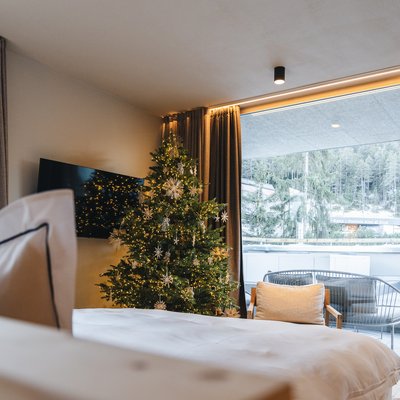 Luxury for the Soul. Nature hotel in South Tyrol. Hotel room with a decorated Christmas tree and balcony view of a snowy forest
