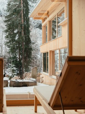 Luxus für die Seele im Kurzurlaub in Südtirol Blick durch Fenster auf schneebedeckten Garten und Holzhaus im Winter