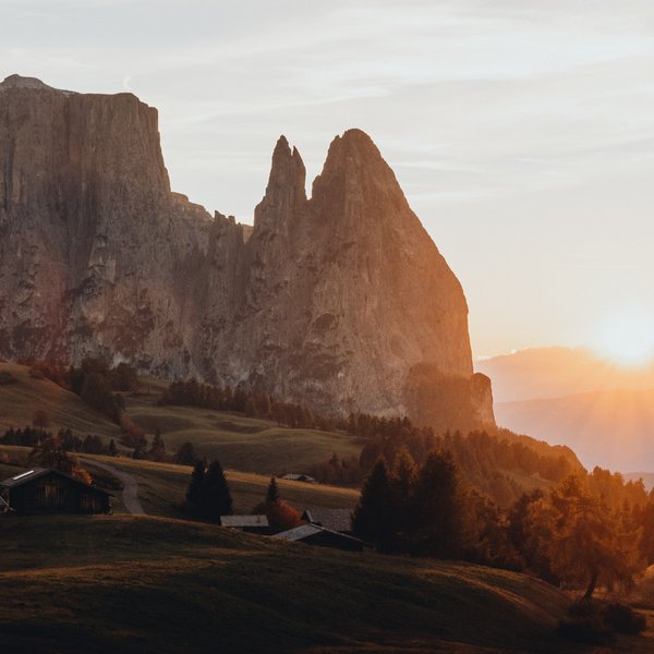 Sensoria Dolomites: Wellnesshotel in den Dolomiten Sonnenuntergang hinter Felsspitzen in einer bergigen Landschaft mit Hütten