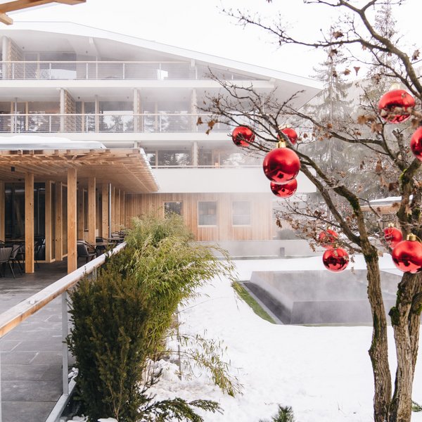 Romantic short break for couples – Sensoria Dolomites Snowy garden with tree decorated with red baubles beside modern wooden building