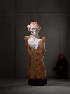 Sensoria Art Edition 01 Modern bust of wood and stone in a dark room, man sitting in the background