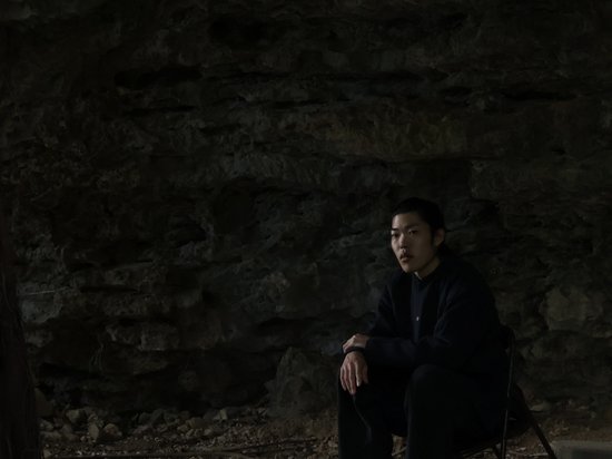 Sensoria Art Edition Junger Mann sitzt in dunkler Felsenhöhle auf Stuhl