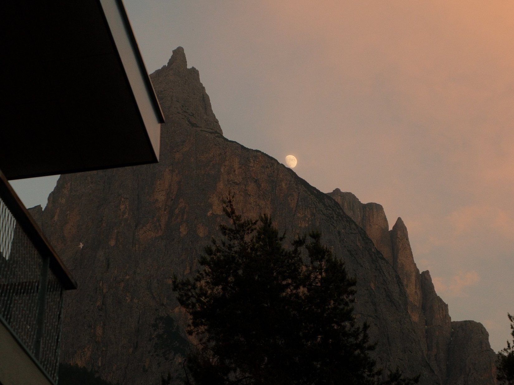 Offers – holidays in the Dolomites UNESCO World Heritage Moon over mountain peak at sunset with building corner in foreground