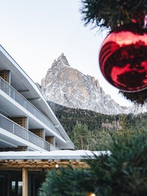 Sensoria Dolomites: il vostro hotel sull’Alpe di Siusi Montagna innevata con edificio moderno e palla di Natale rossa in primo piano