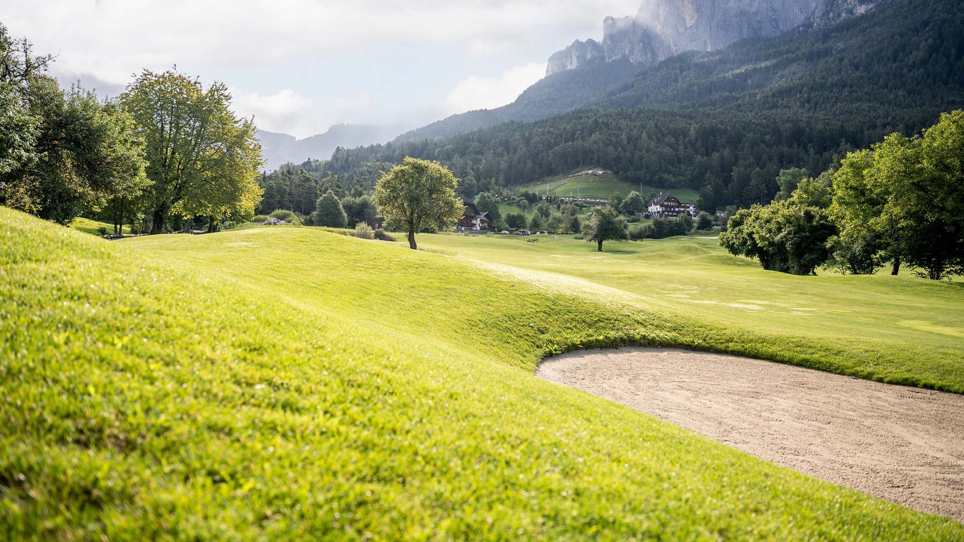 Vacanza e golf: accoppiata vincente Campo da golf verde con ostacolo di sabbia e montagne sullo sfondo