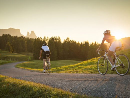 A summer holiday in the mountains Two cyclists riding on a country road at sunset through a green landscape.