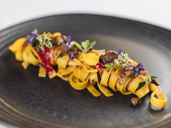 Naturhotel in Südtirol. Luxus für die Seele. Elegante Tagliatelle mit Sauce und essbaren Blüten auf schwarzem Teller