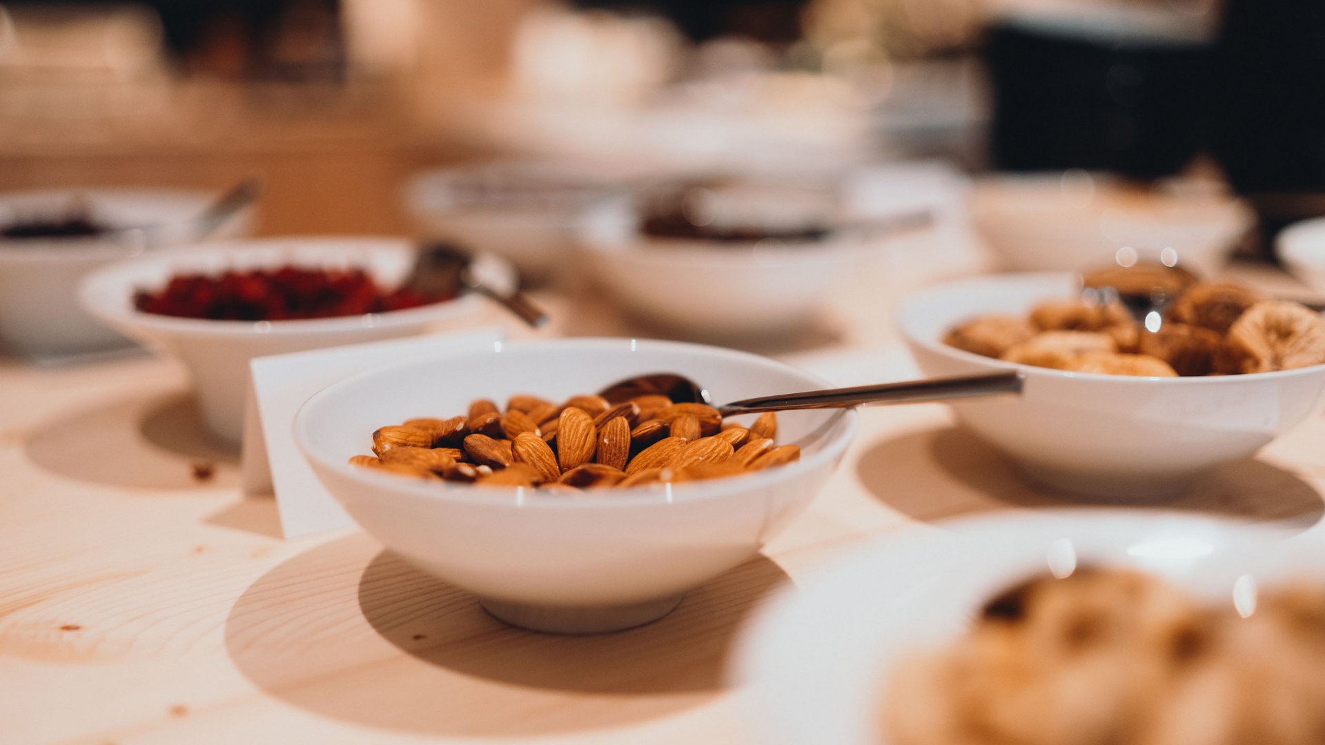 Unser Genussmarkt – perfekt für Ihr Romantikwochenende Weiße Schale mit Mandeln auf einem Holztisch mit anderen Schalen im Hintergrund