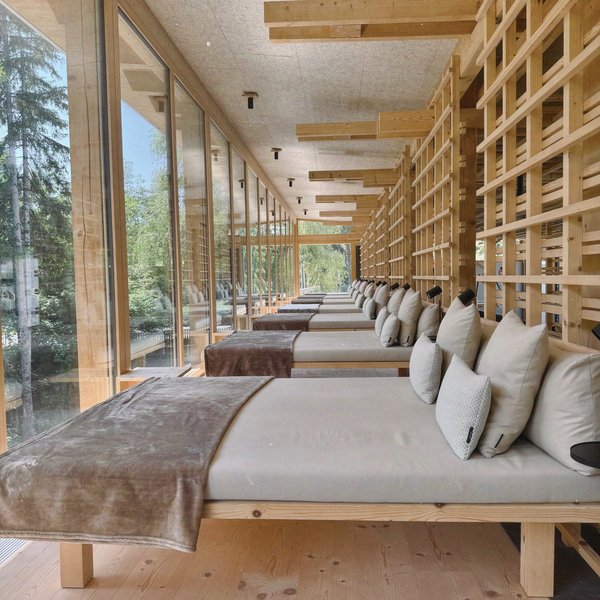 From hiking on Alpe di Siusi/Seiser Alm to the spa area Row of loungers with pillows in a modern wooden room with large windows
