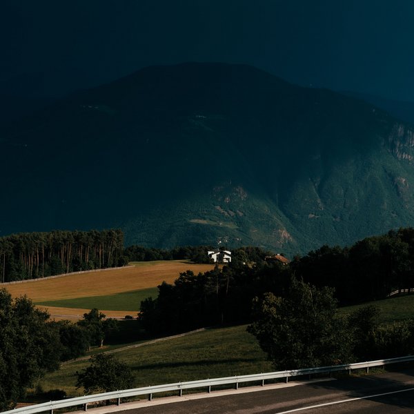 Active holidays in South Tyrol – ready for pure nature? Curved country road with fields and mountains in the background under dark sky