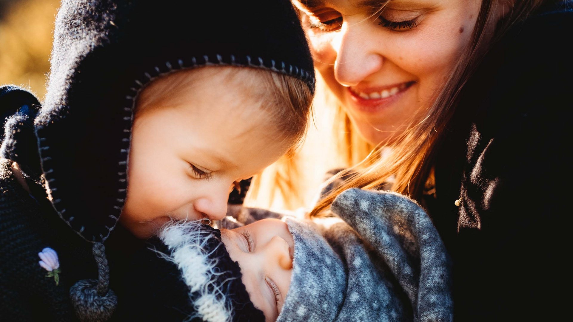 Places of spiritual power, favourite rooms, hosts with heart Child tenderly kisses a swaddled baby held by smiling mother