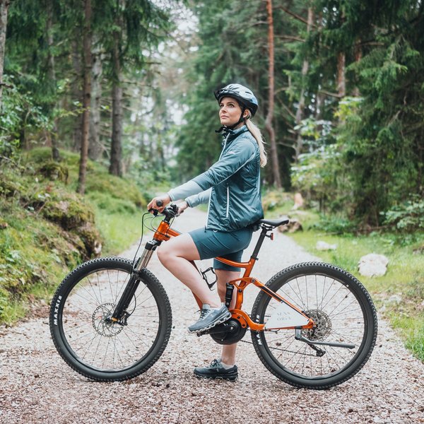 Sensoria Dolomites: Wellnesshotel in den Dolomiten Frau mit Helm auf orangefarbenem Mountainbike auf Waldweg