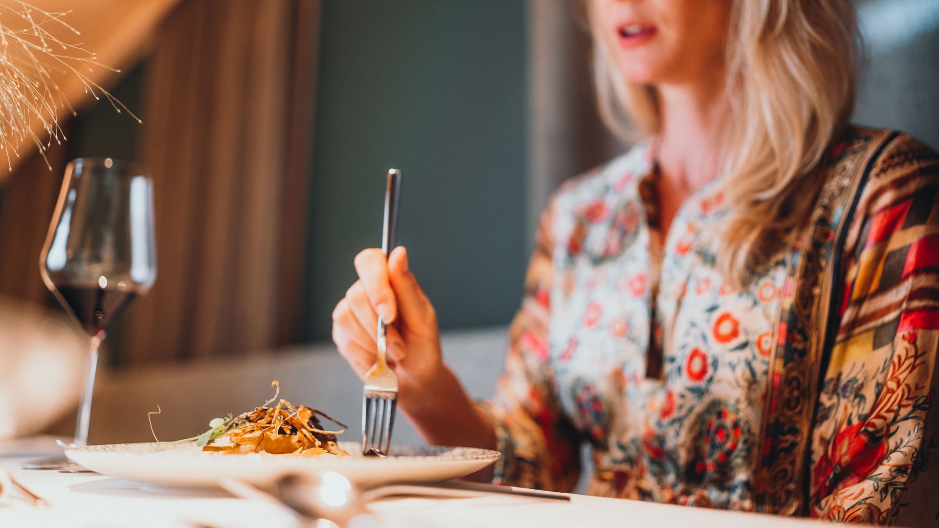 Inklusivleistungen – last minute nach Südtirol Frau isst in elegantem Restaurant mit Weinglas und feinem Essen.